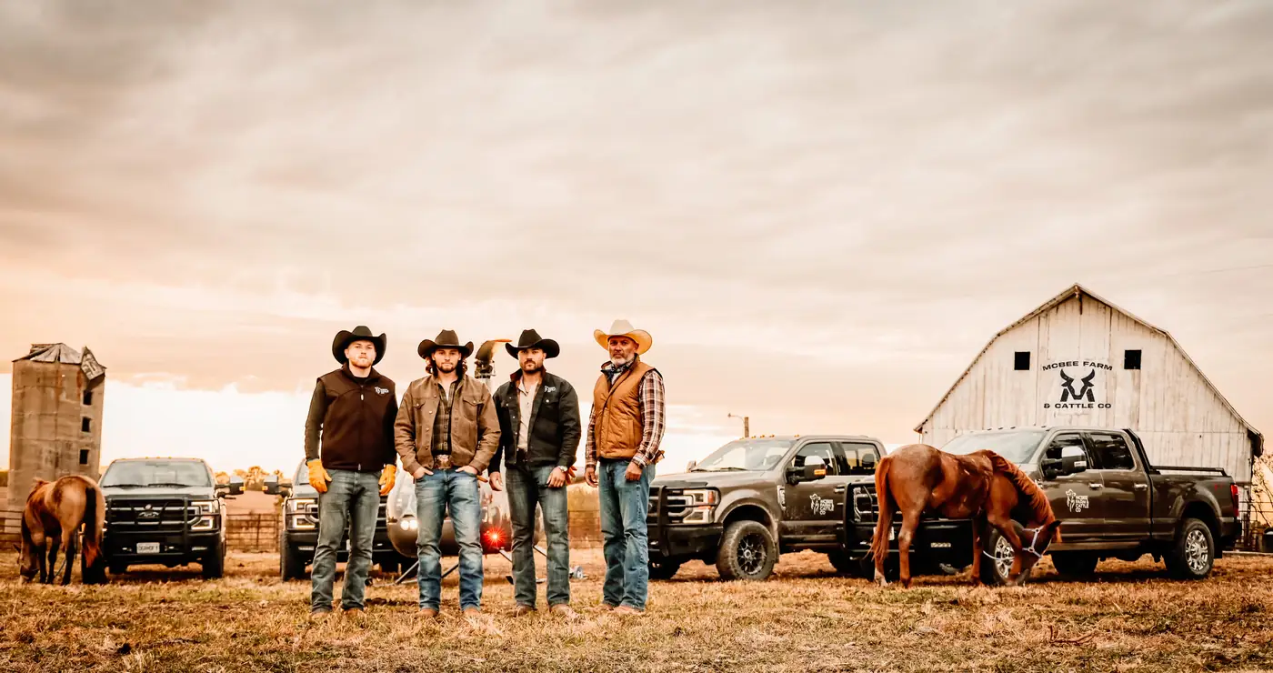 The McBee men standing in front of the McBee Farm & Cattle Co. barn and trucks